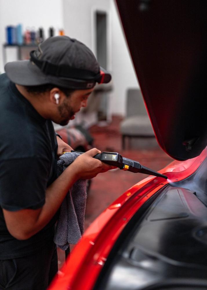 Obsidian detailer machine-polishing a supercar in the bay