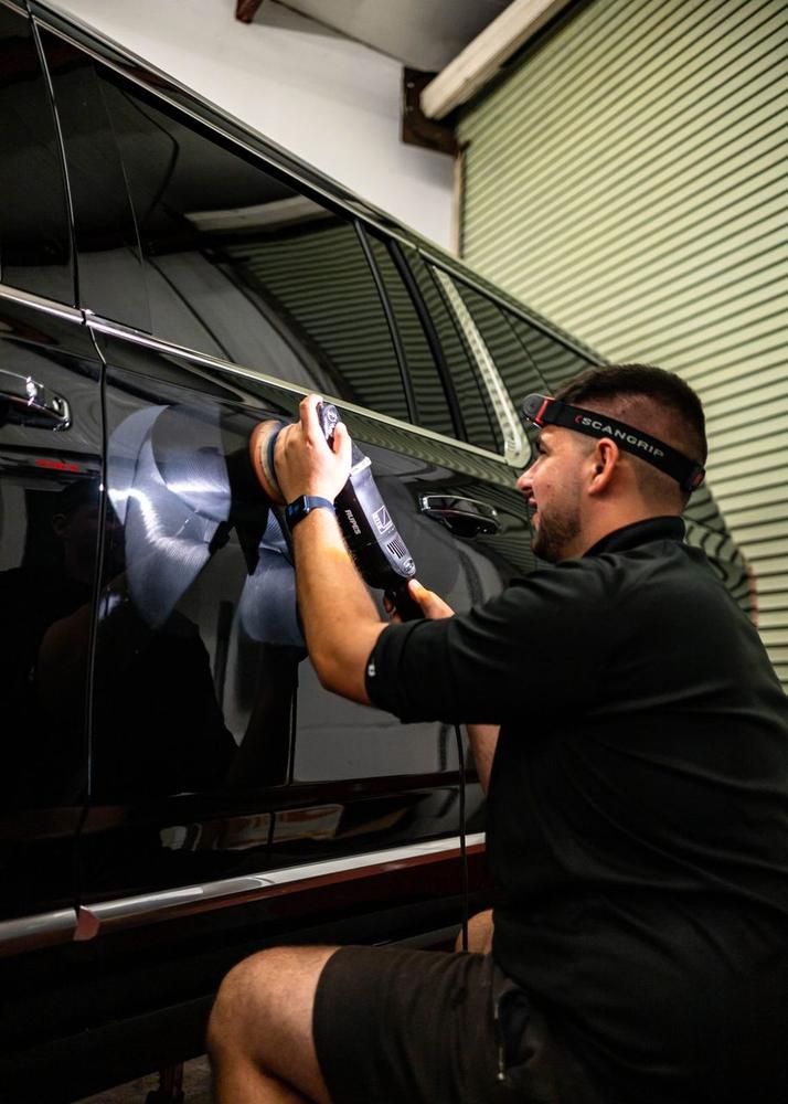 Obsidian detailer machine-polishing a black SUV in the studio